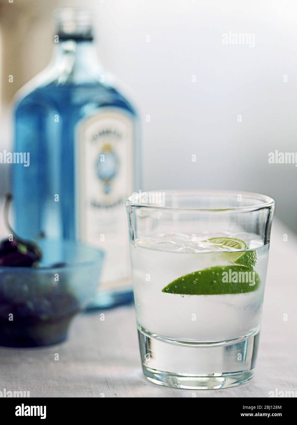 Glass of gin and tonic with lime segment and bottle of Bombay Sapphire in background - Stock Photo