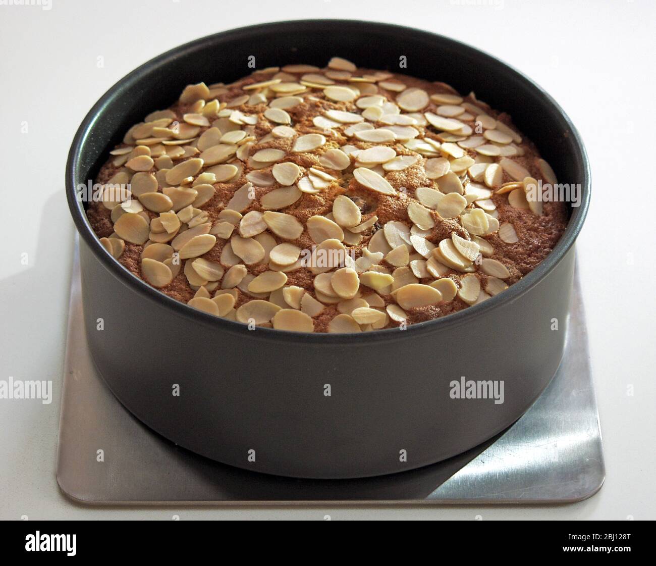 Light fruit cake topped with almonds in tin - Stock Photo
