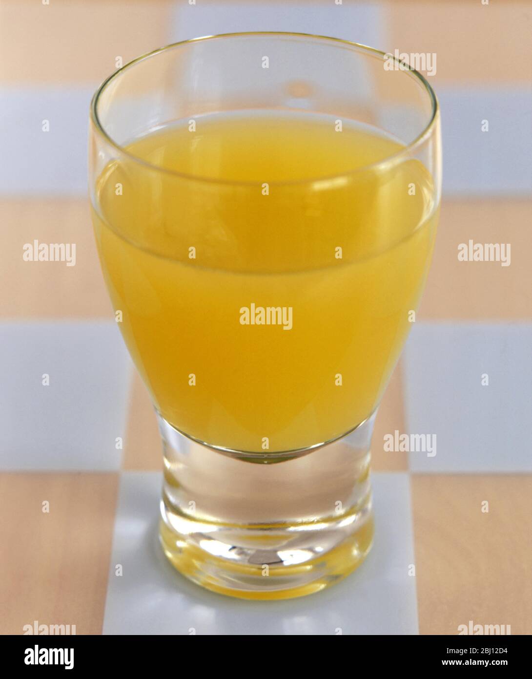 Glass of orange juice on checked placemat - Stock Photo