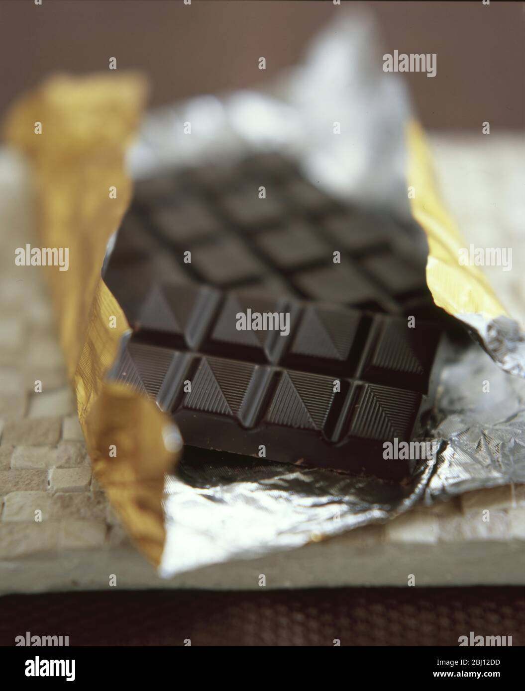 Dark chocolate bar opened and sitting in foil wrapping - Stock Photo