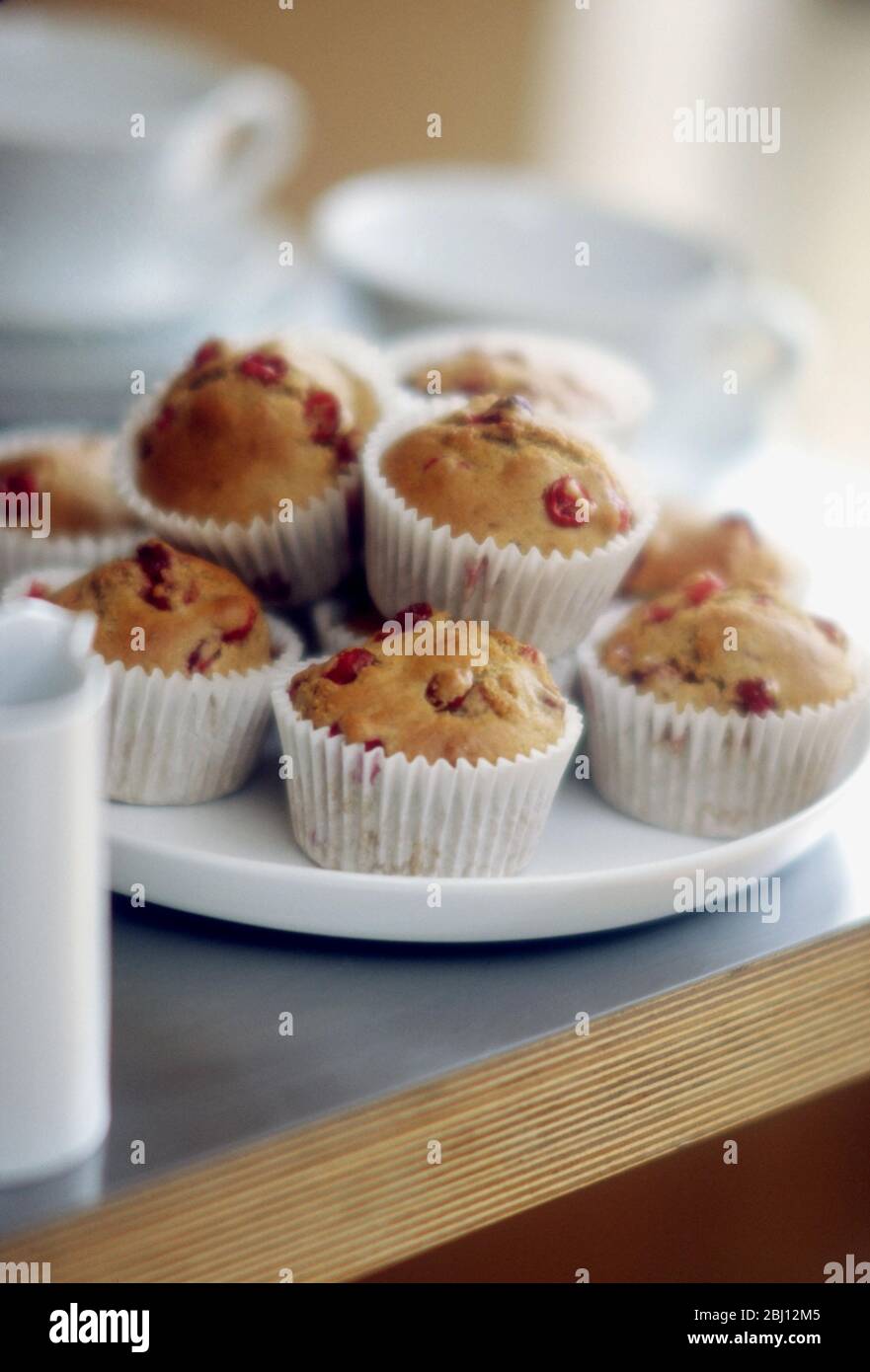 Plate of muffins in paper cases in teatime setting - Stock Photo