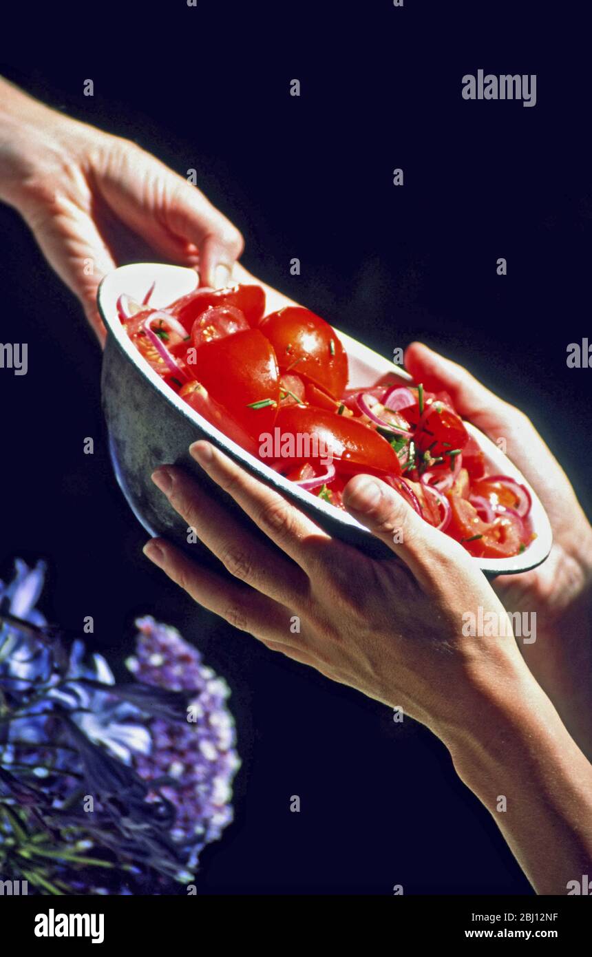 Bowl of tomato sald being passed between hands - Stock Photo