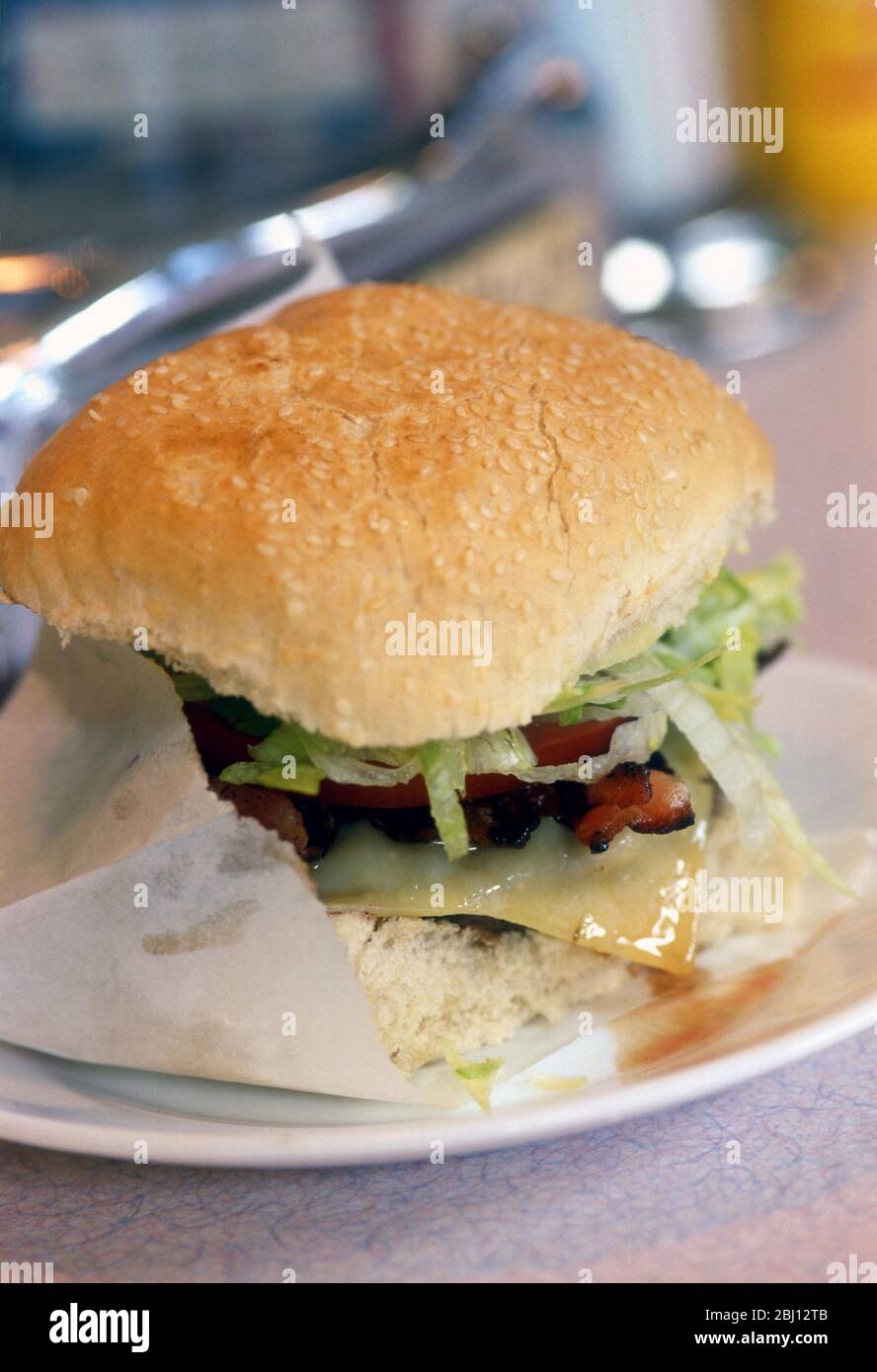 BLT burger in sesame bun in paper bag on white plate on counter of classic american style diner - Stock Photo