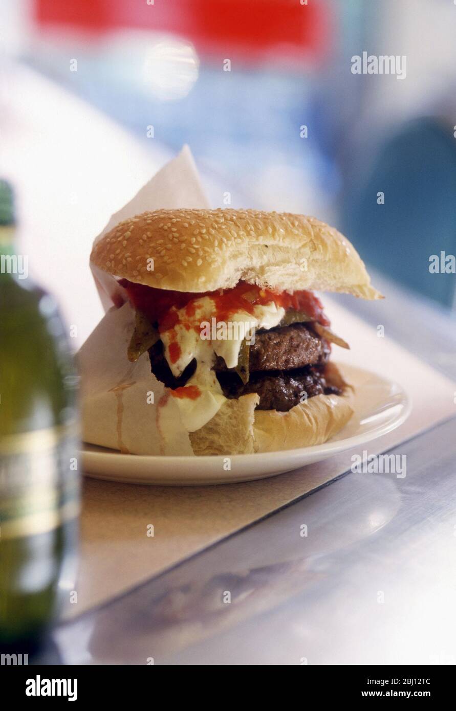 Classic double cheeseburger with melting cheese and ketchup in paper bag on white plate on counter of American style diner - Stock Photo
