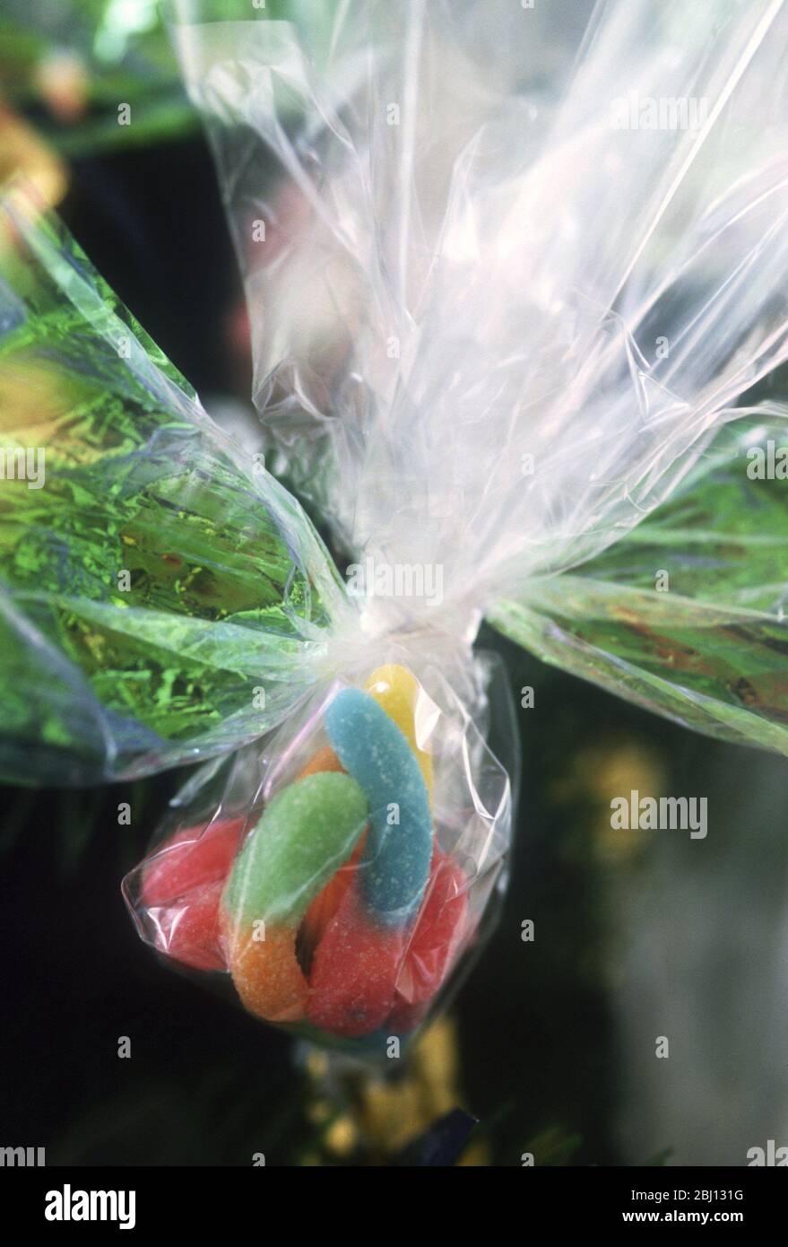 Sweets tied up in a net bundle and hanging as decoration on a Christmas tree - Stock Photo