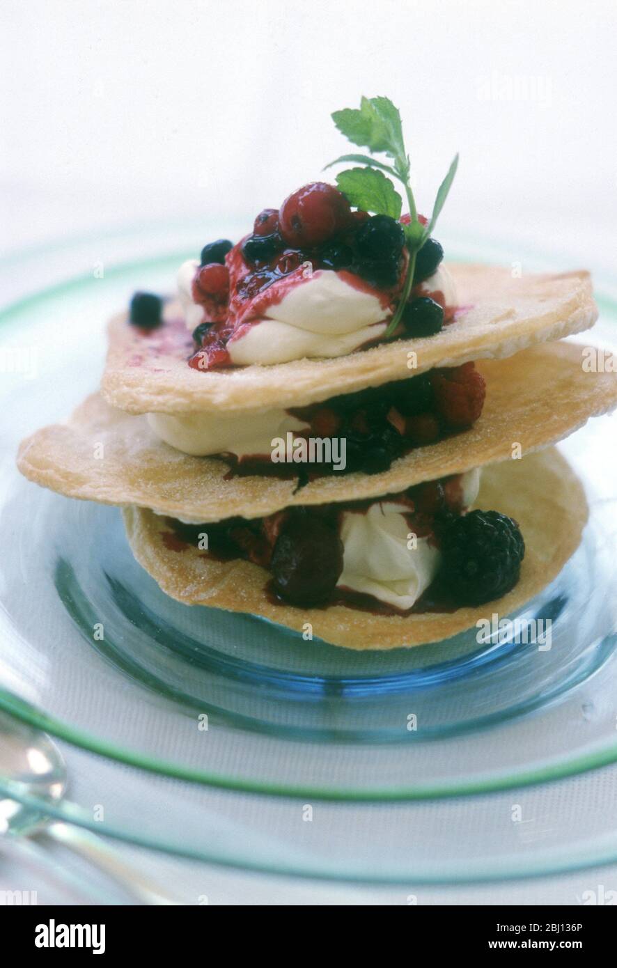 Mille feuilles pastry with whipped cream and summer berries, garnished with mint sprig. - Stock Photo