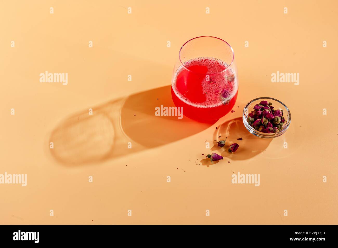 https://c8.alamy.com/comp/2BJ13JD/pink-alcoholic-cocktail-with-lemonade-champagne-or-martini-decorated-with-dry-rosebuds-on-colored-background-with-glare-in-the-background-2BJ13JD.jpg