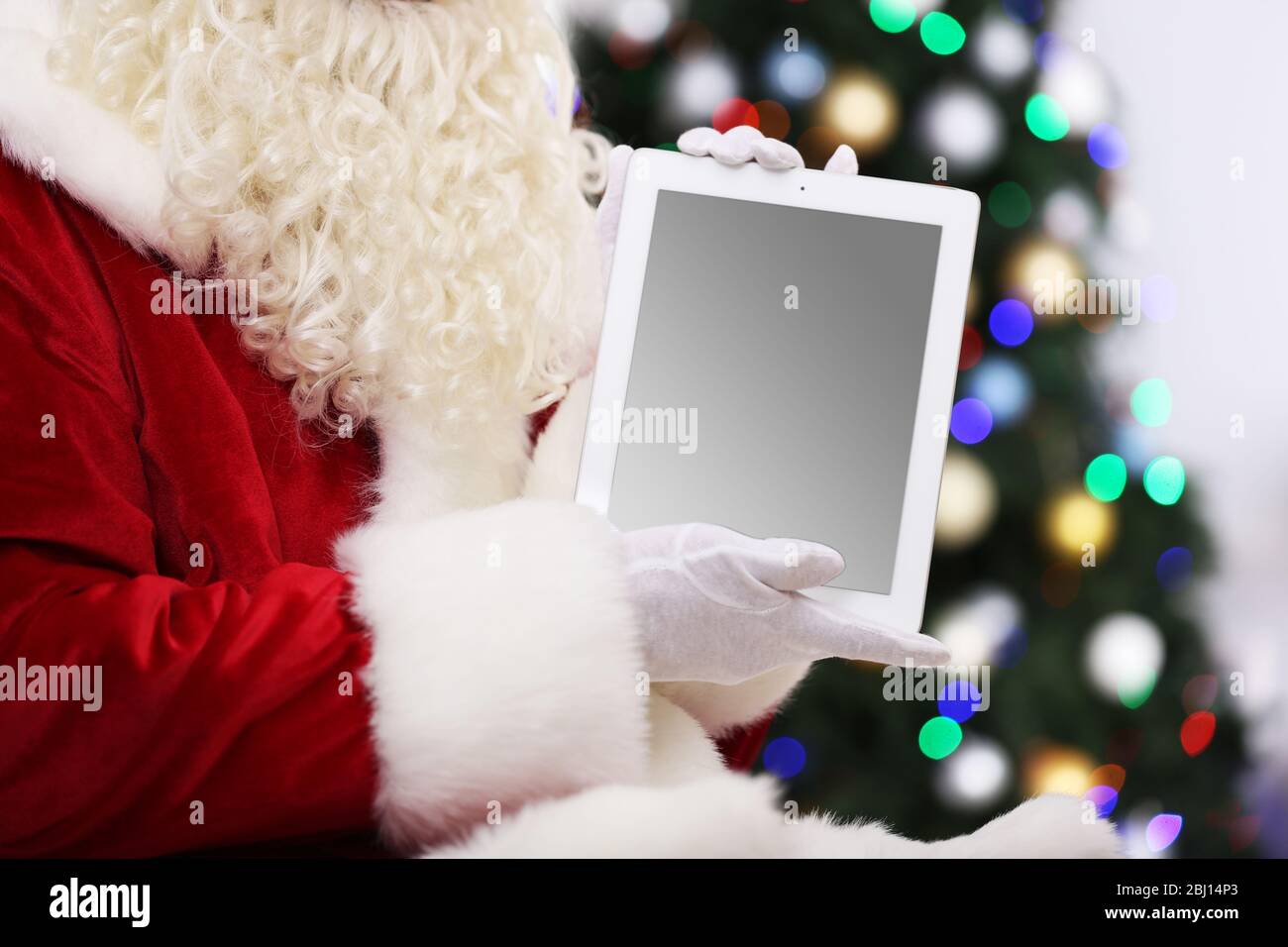 Santa holding tablet on Christmas tree background Stock Photo - Alamy