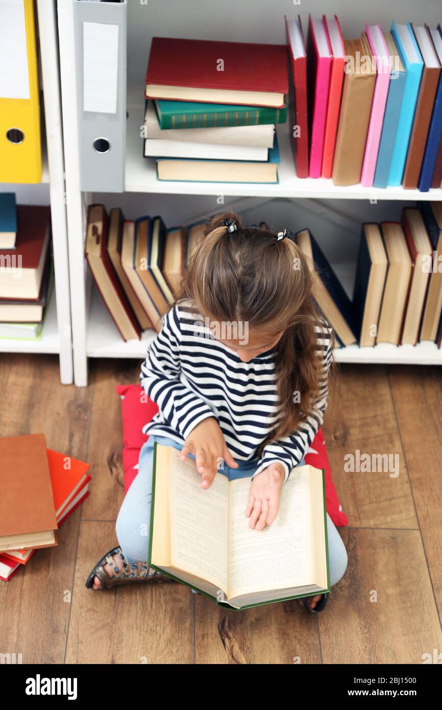Beautiful little girl with books sitting on floor in library Stock ...