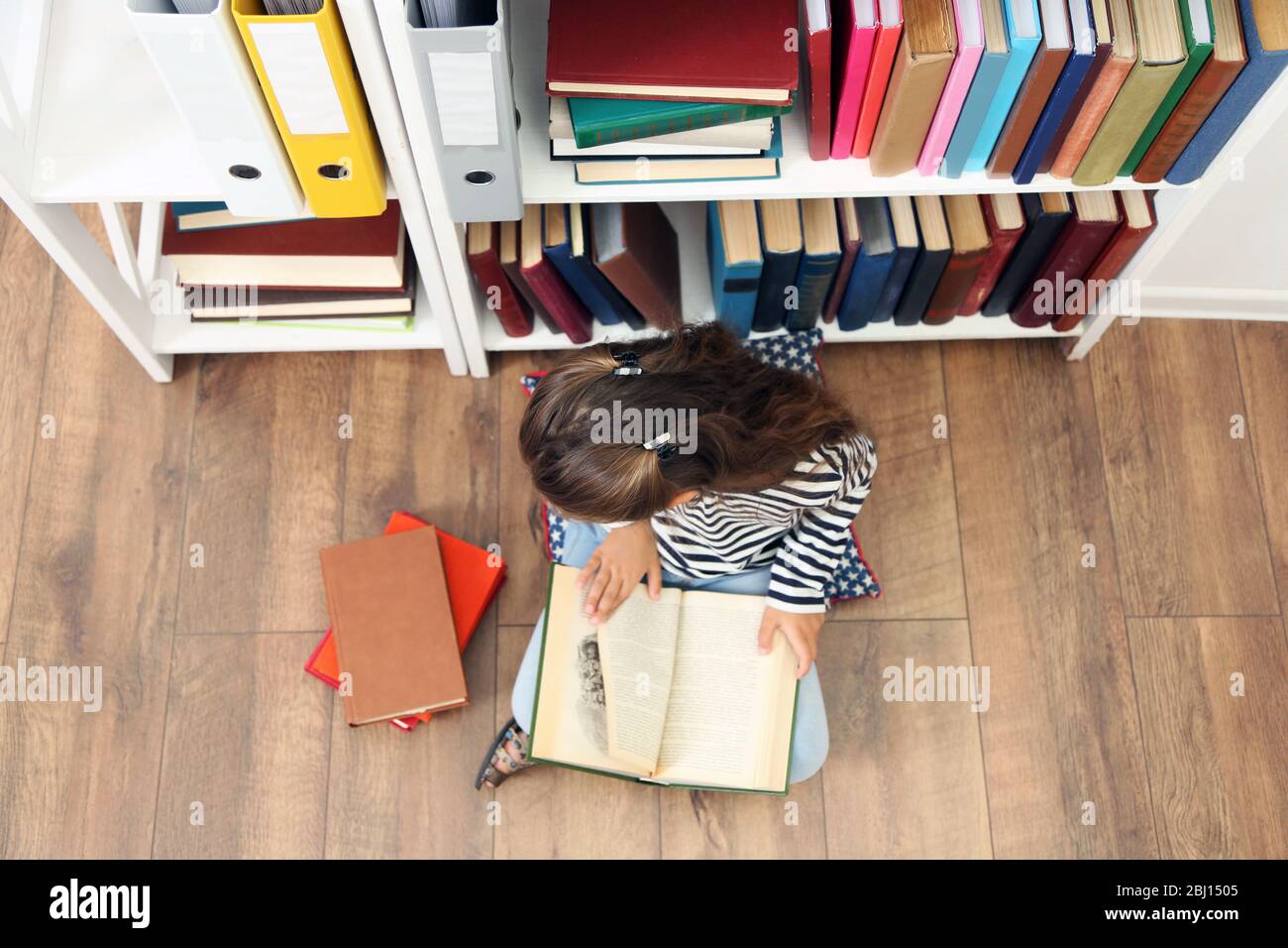 Beautiful little girl with books sitting on floor in library Stock ...