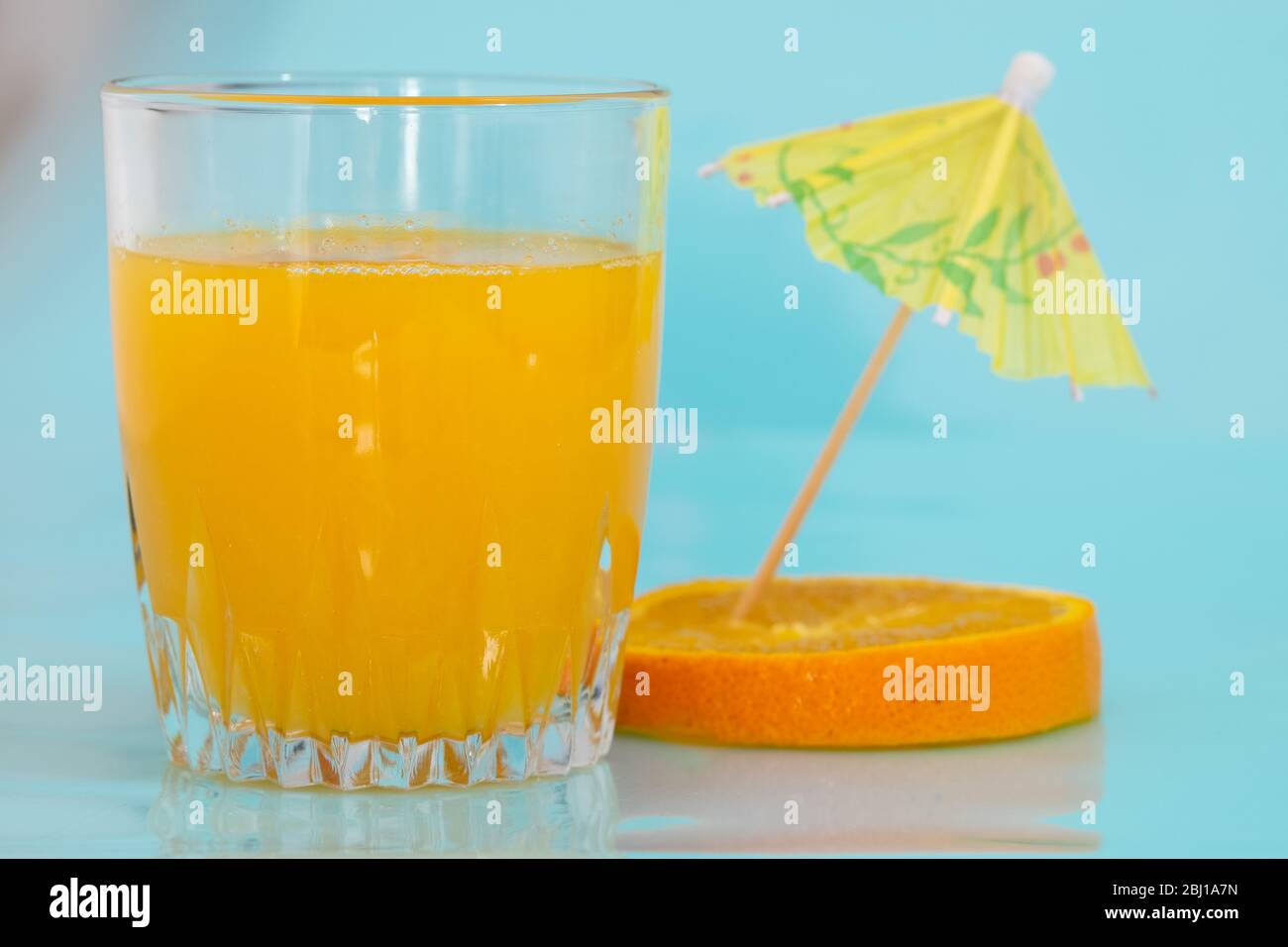 Vitamin Crich orange juice is near an orange slice and an umbrella