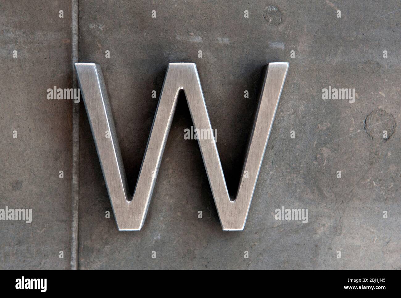 A Close Up Of The Letter W In Metal Against A Grey Stone Wall Stock Photo