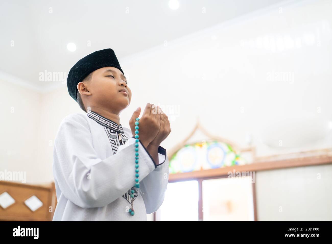 boy praying to god with arm open holding prayer beads in the mosque ...