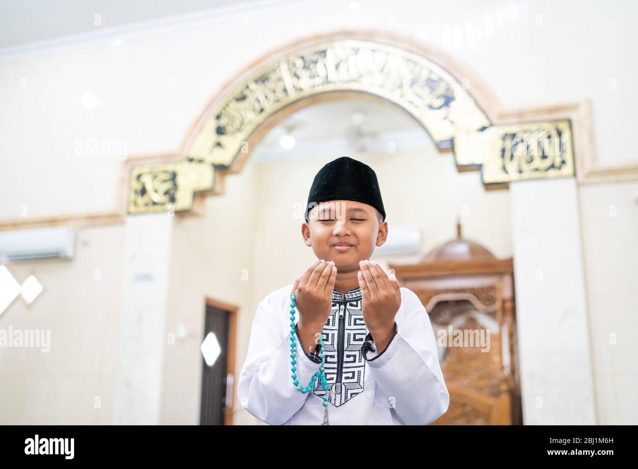 boy praying to god with arm open holding prayer beads in the mosque ...