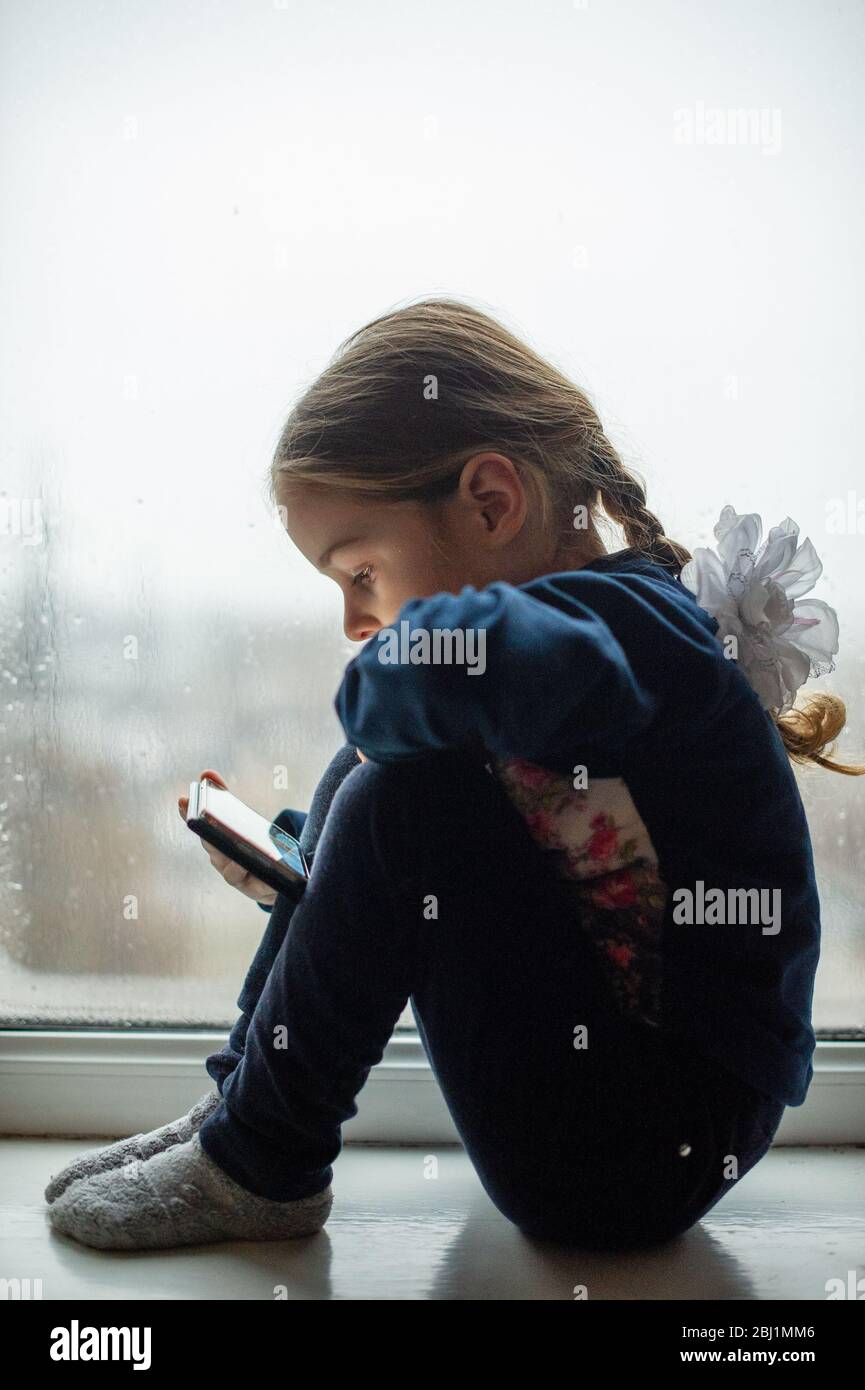 Beautiful cute female kid with sitting on windowsill. A little girl ...