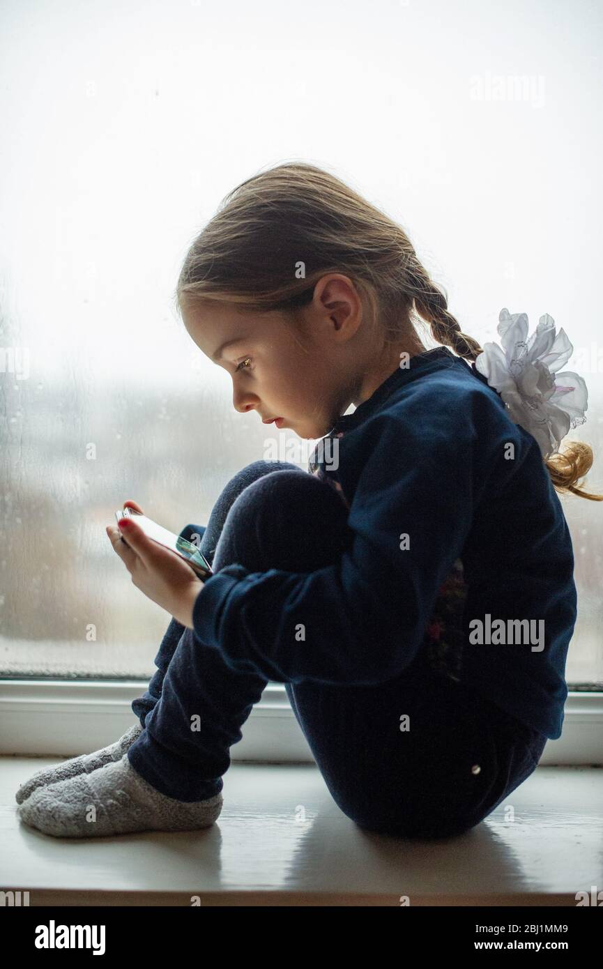 Beautiful cute female kid with sitting on windowsill. A little girl ...