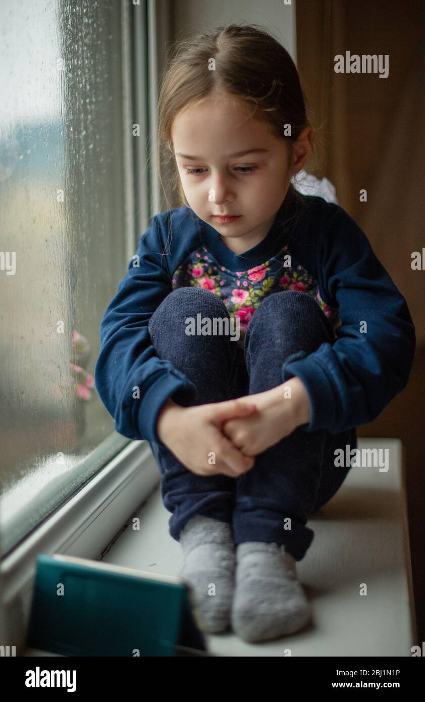 Beautiful cute female kid with sitting on windowsill. A little girl ...