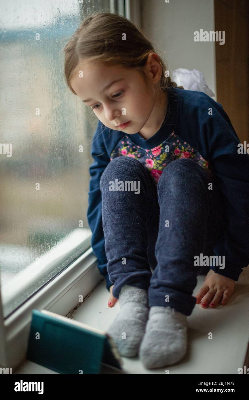 Beautiful cute female kid with sitting on windowsill. A little girl ...