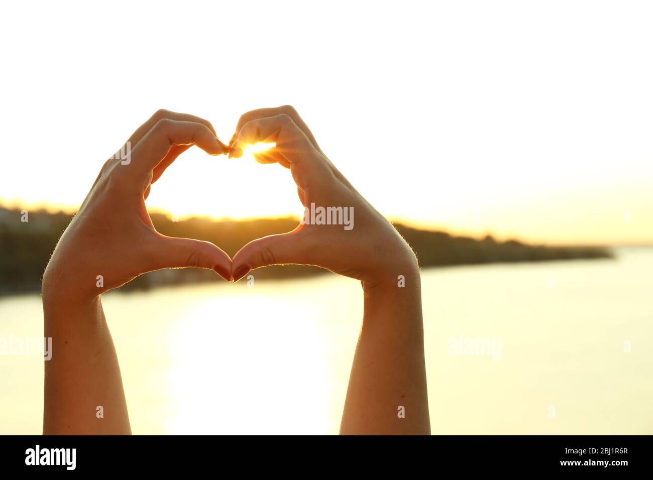 Female hands in shape of heart on sunny sky background Stock Photo - Alamy