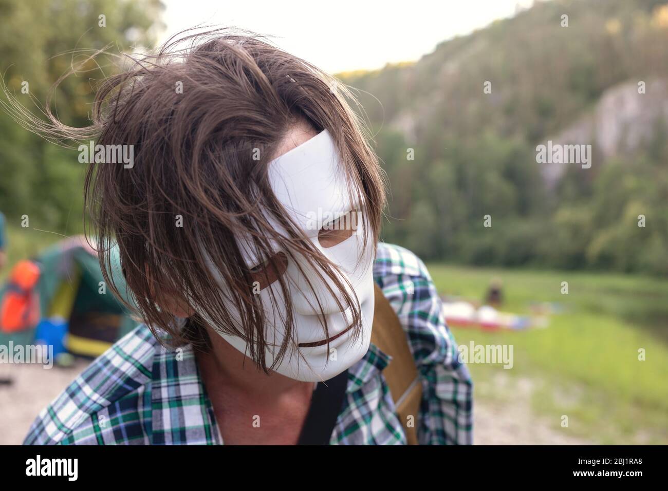 Close up portrait of man with dishelved hair hiding face under white  plastic mask on blurred natural background. Anonymous, in disguise,  thriller, lif Stock Photo - Alamy