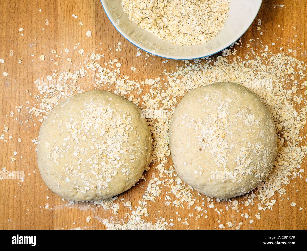 Two rounds of oat bread dough rolled in oats on a wooden kitchen table with a bowl of oats Stock Photo