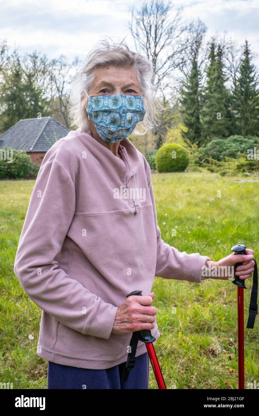 Seniorin mit Walking-Stöcken als Gehhilfe in der Natur mit Maske. Die Seniorin trägt einen Mundschutz. Stock Photo