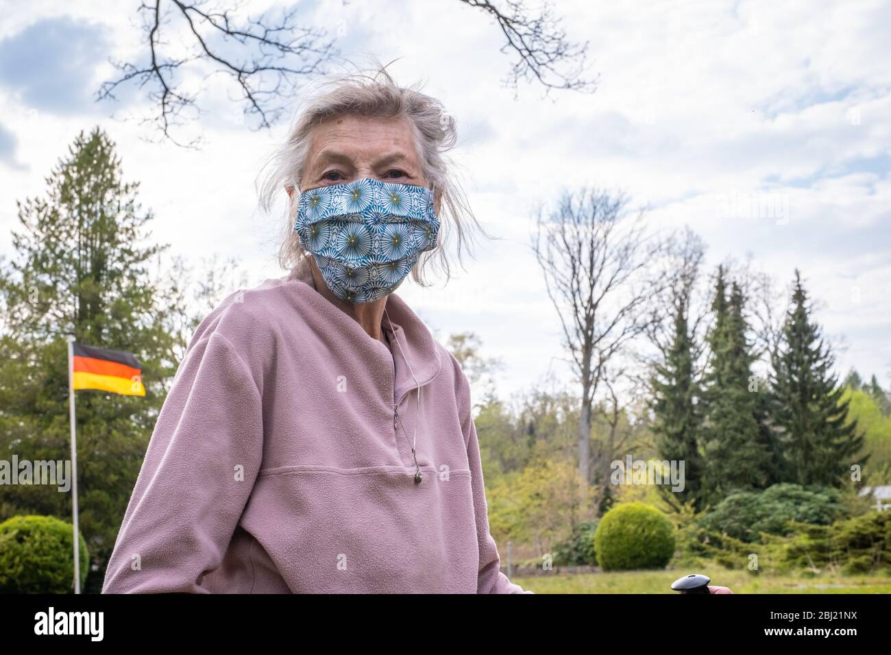 Seniorin mit Walking-Stöcken als Gehhilfe in der Natur mit Maske. Die Seniorin trägt einen Mundschutz. Stock Photo