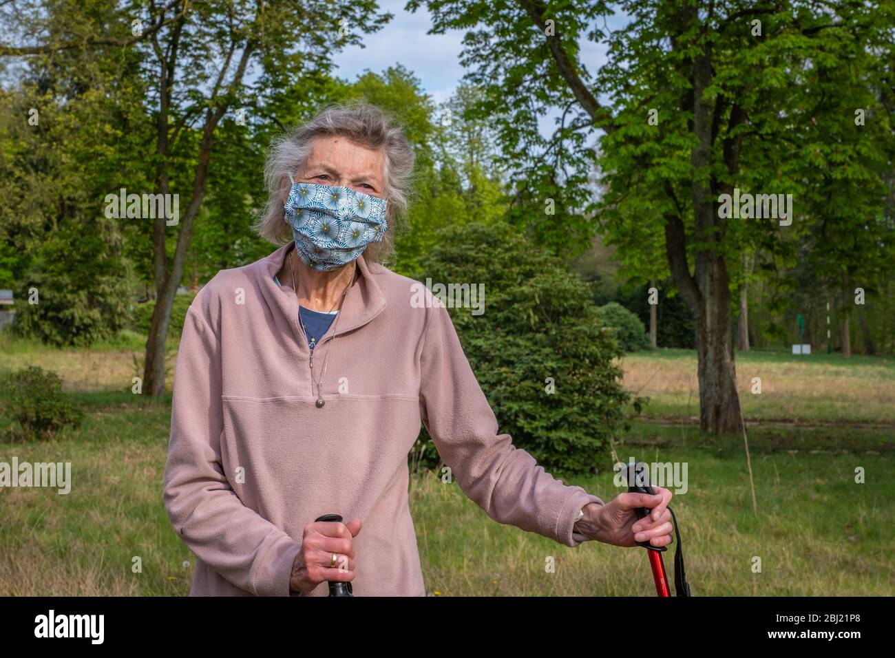 a woman with grey hair ties up her face mask outside Stock Photo