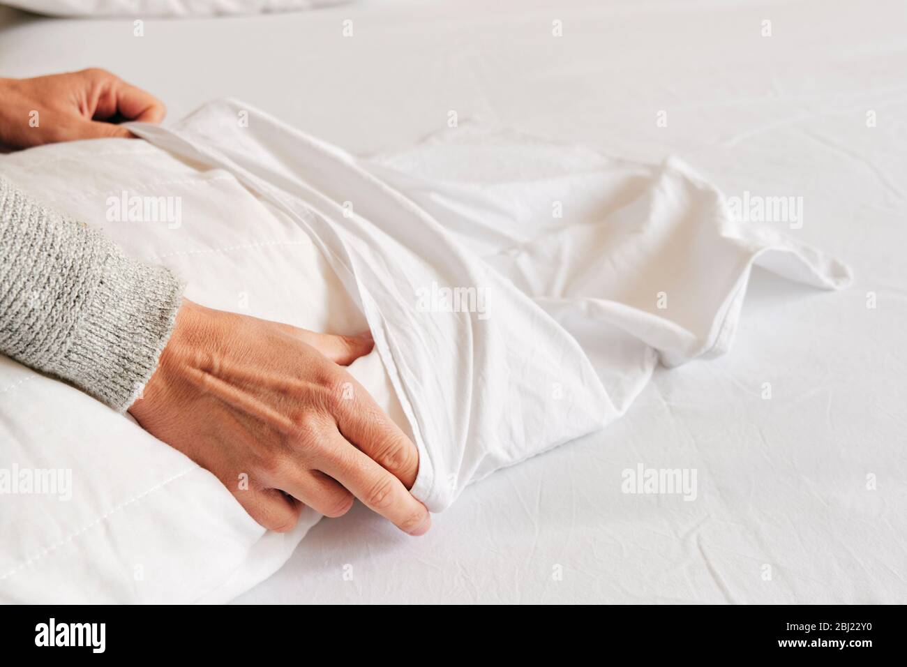closeup of a young caucasian man introducing a pillow into a white pillow case as he is making the bed Stock Photo