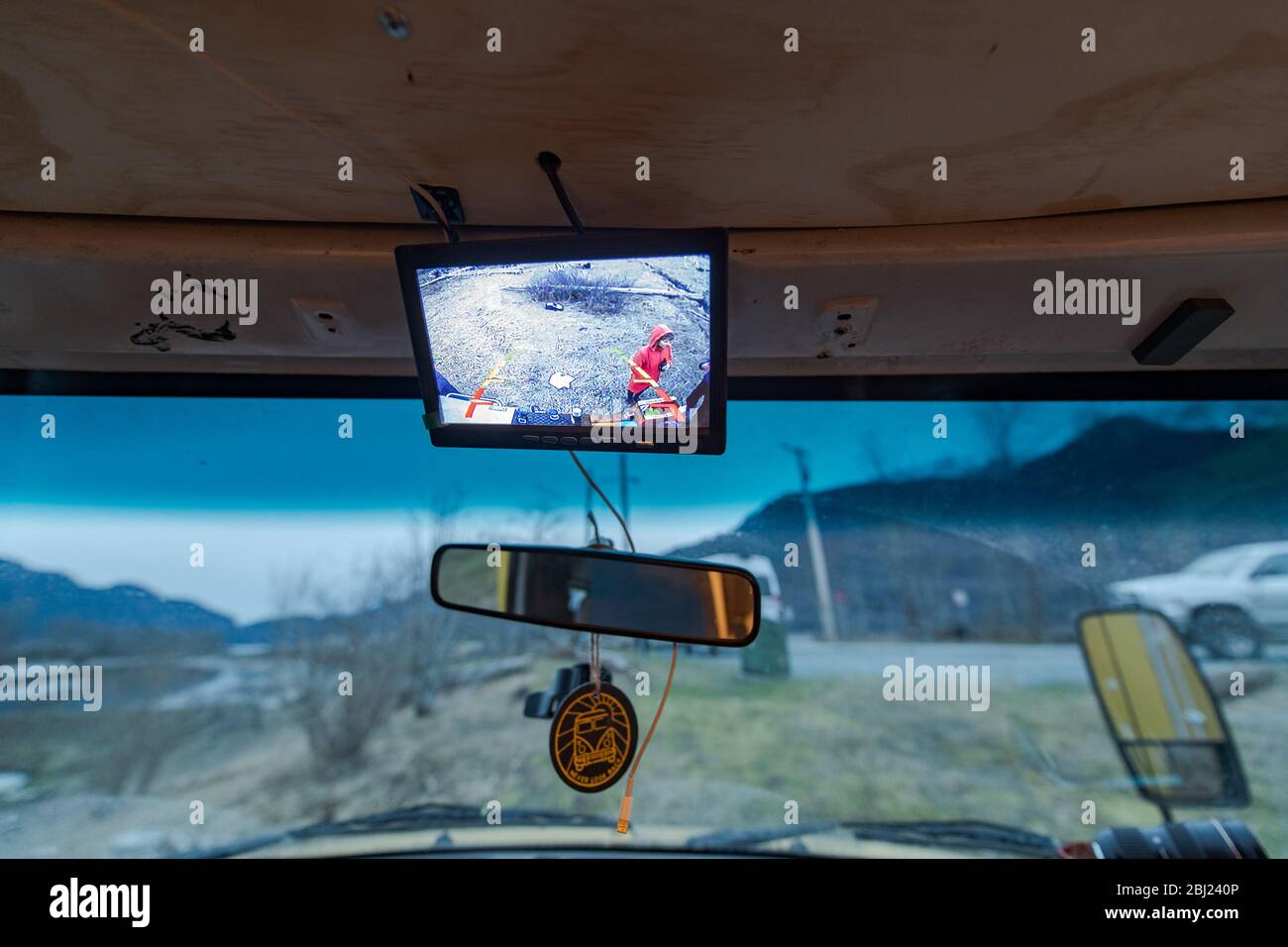 Campervan parked, view through windscreen of wet weather and rocky landscape, one person visible in mirror. Stock Photo