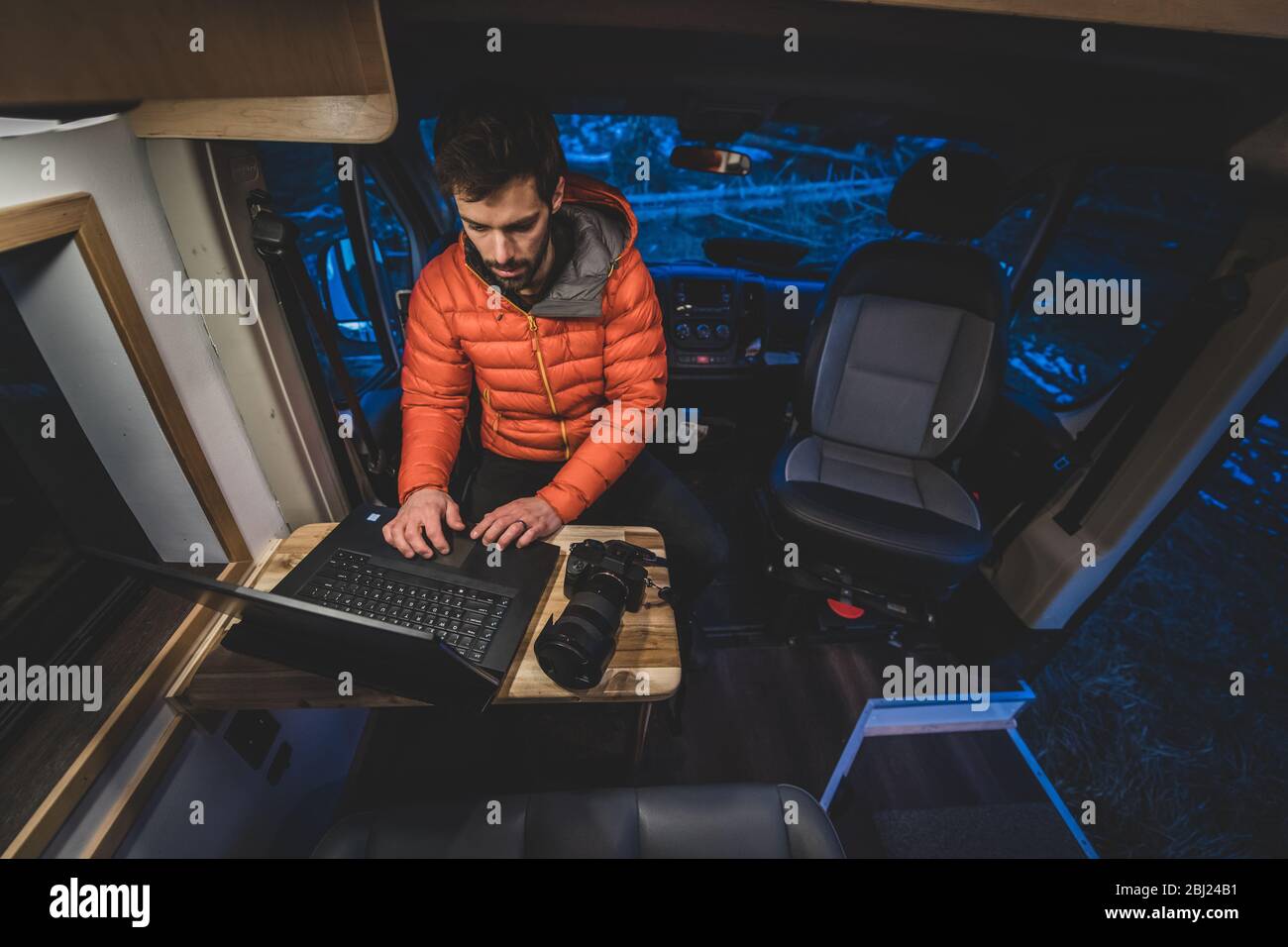 A man sitting at a wooden table in his campervan working on his laptop. Stock Photo