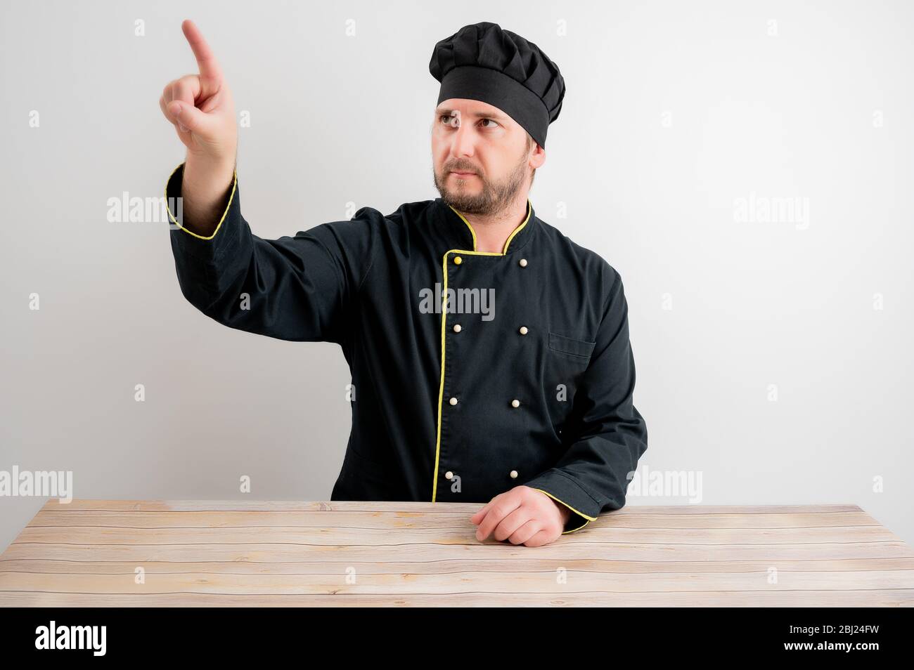 Young male chef in black uniform presses a virtual button posing on a white isolated background Stock Photo