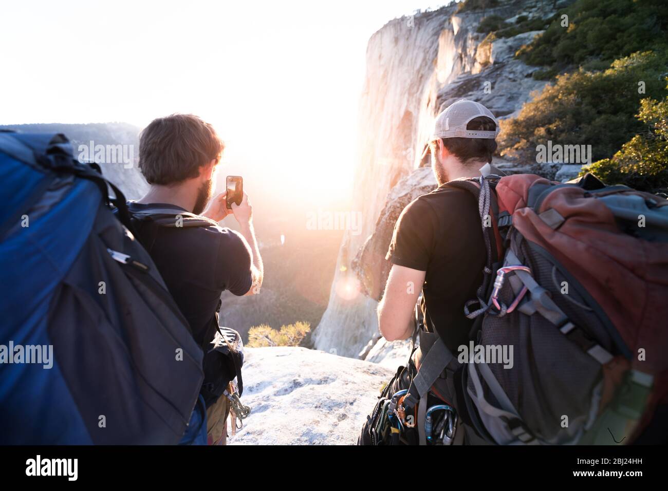 Rear view of two men taking pictures of rocks and a sunset with a mobile phone. Stock Photo