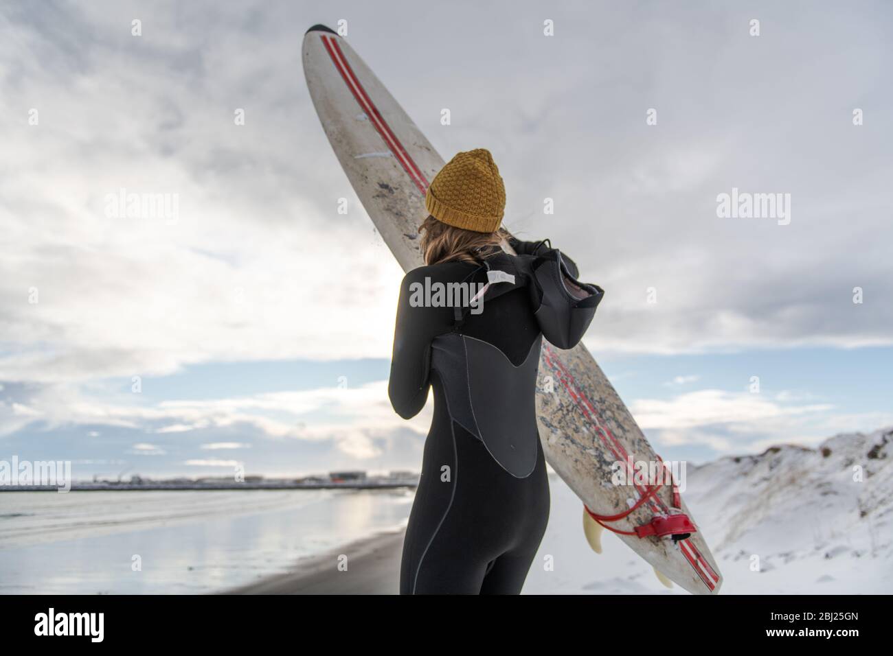 Rear view of a woman wearing a wetsuit and holding a surfboard standing