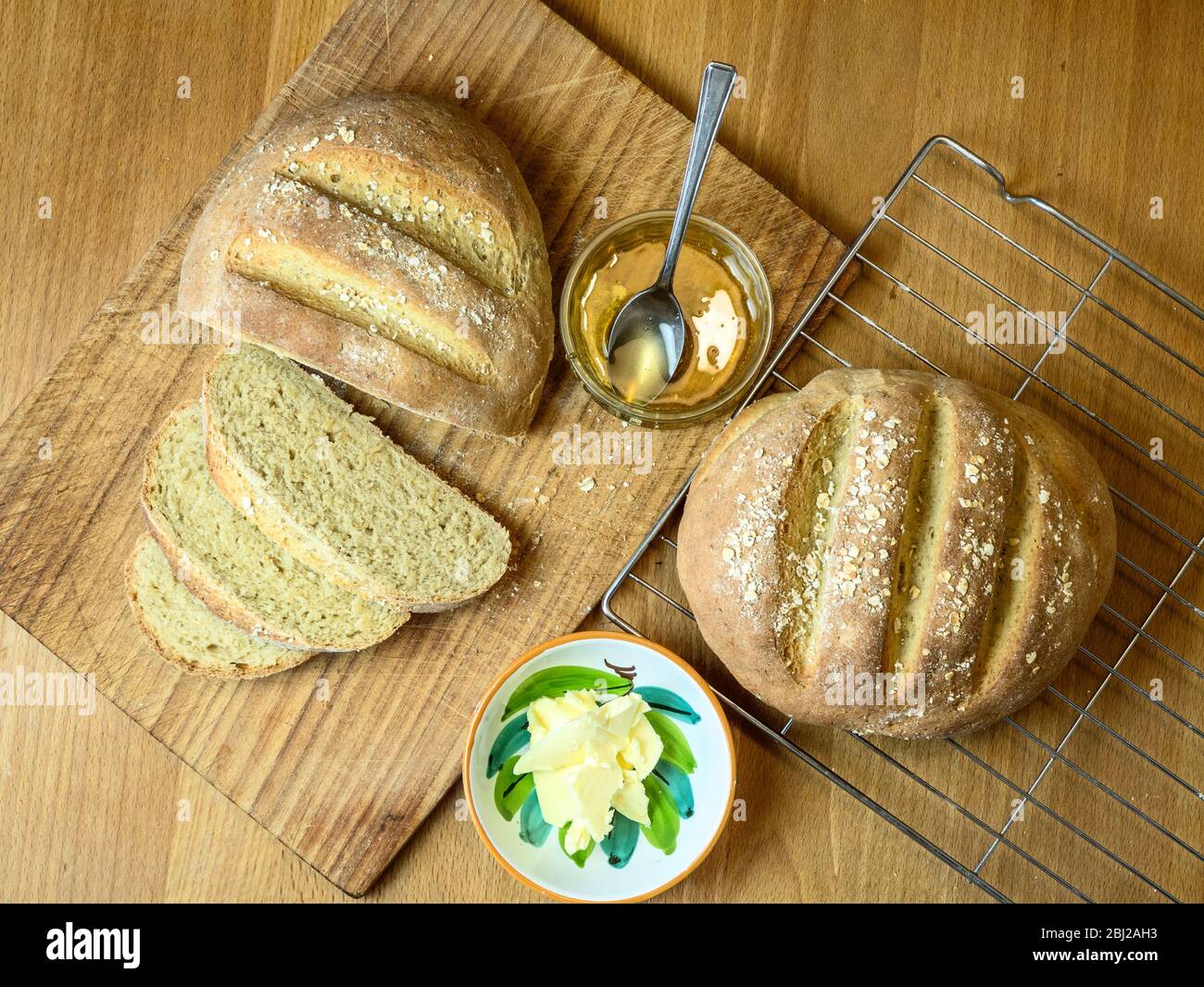 Freshly baked oat bread made with white bread flour and oat flour topped with rolled oats with honey and non dairy spread Stock Photo