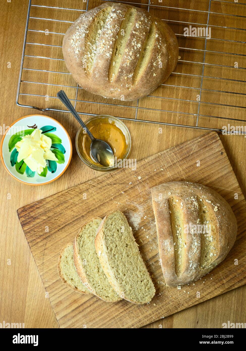 Freshly baked oat bread made with white bread flour and oat flour topped with rolled oats with honey and non dairy spread Stock Photo