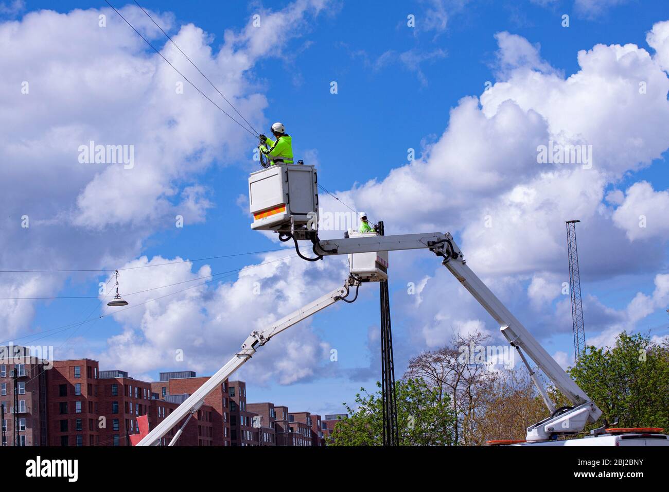 Lineworkers working on power lines in crane buckets high in the air from aerial lift. He is wearing yellow fluorescent clothes for safety. A sunny day Stock Photo