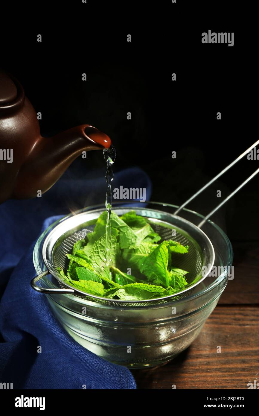 Making mint icecream. Pouring hot water through sieve with mint leaves