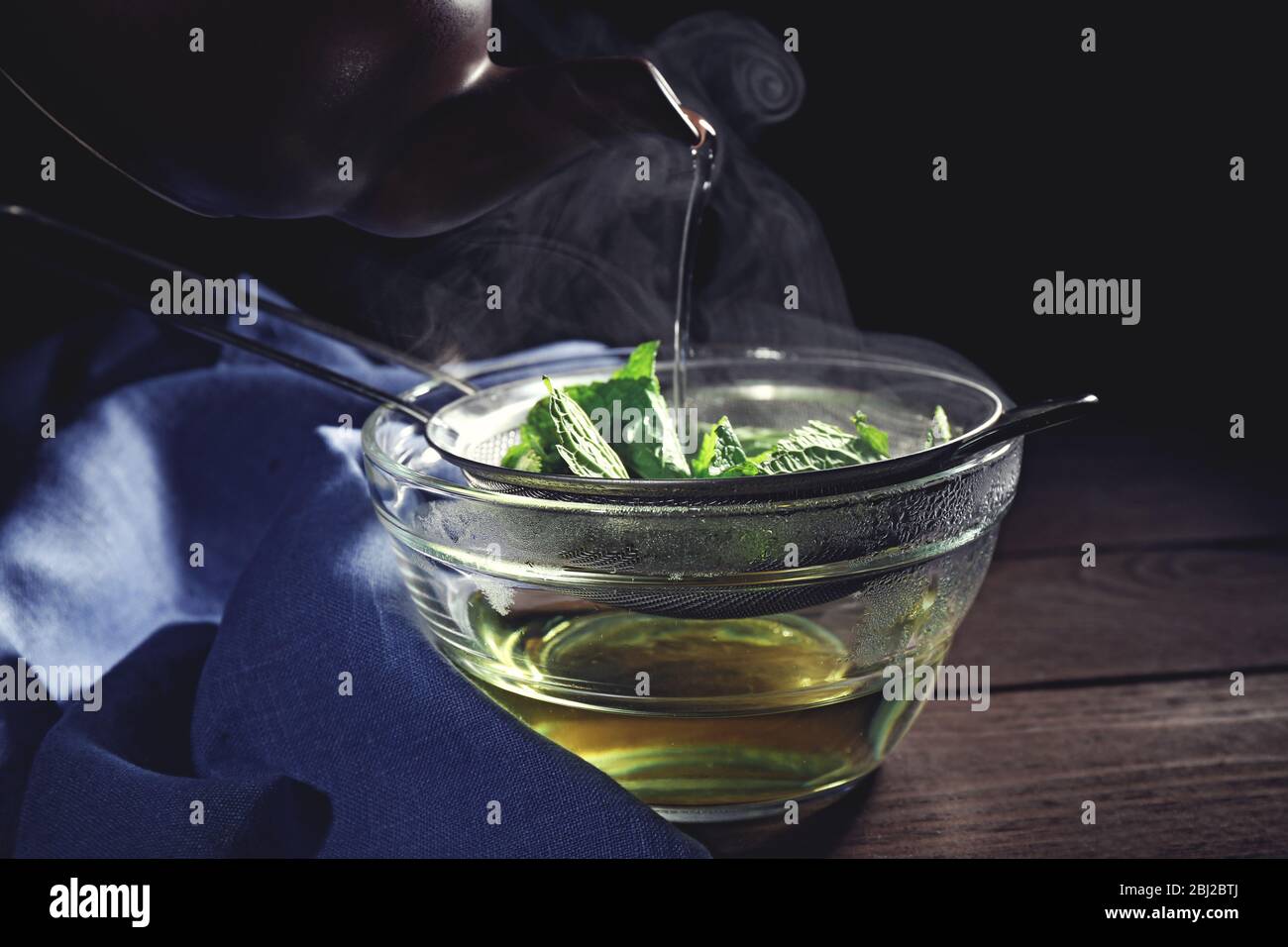 Making mint icecream. Pouring hot water through sieve with mint leaves