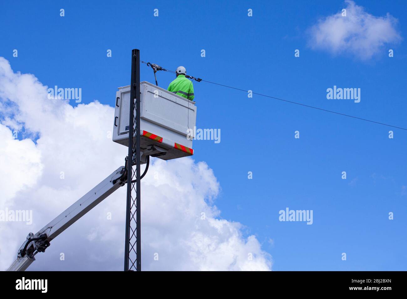 Lineworker working on power lines in crane bucket in the air from