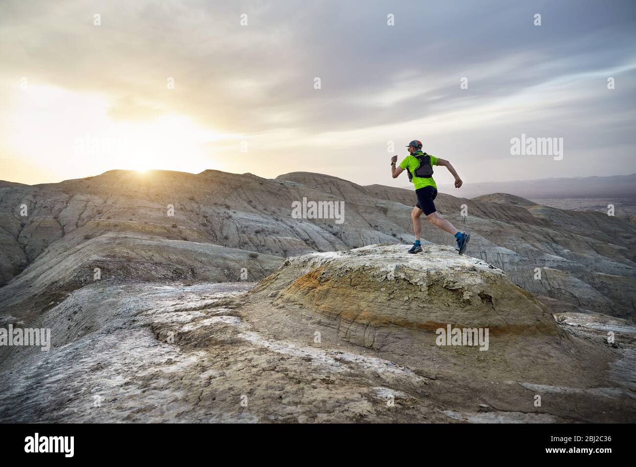 Runner athlete with backpack running on the wild mountains in the desert at sunset Stock Photo
