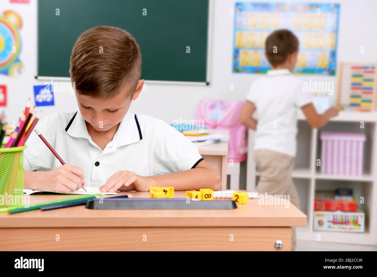 Little boy drawing at the desk in classroom Stock Photo - Alamy