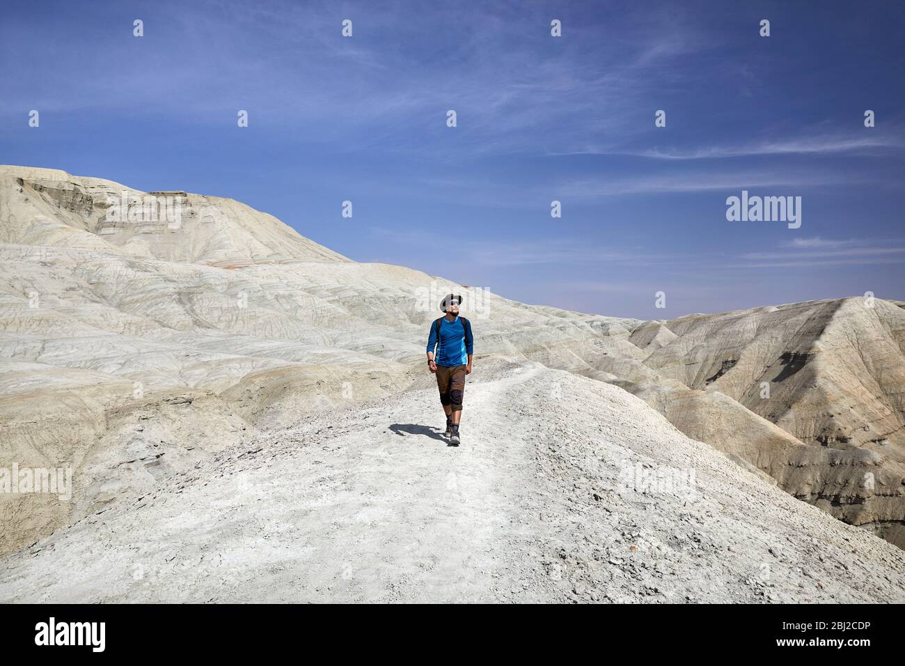 Tourist in hat walking at the trail on surreal white mountains against blue sky in desert park Altyn Emel in Kazakhstan Stock Photo