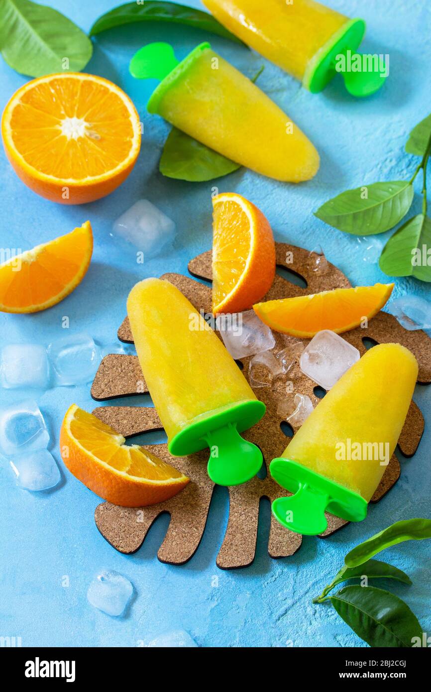 Homemade popsicles with orange juice, fruit ice, lollipops on a blue