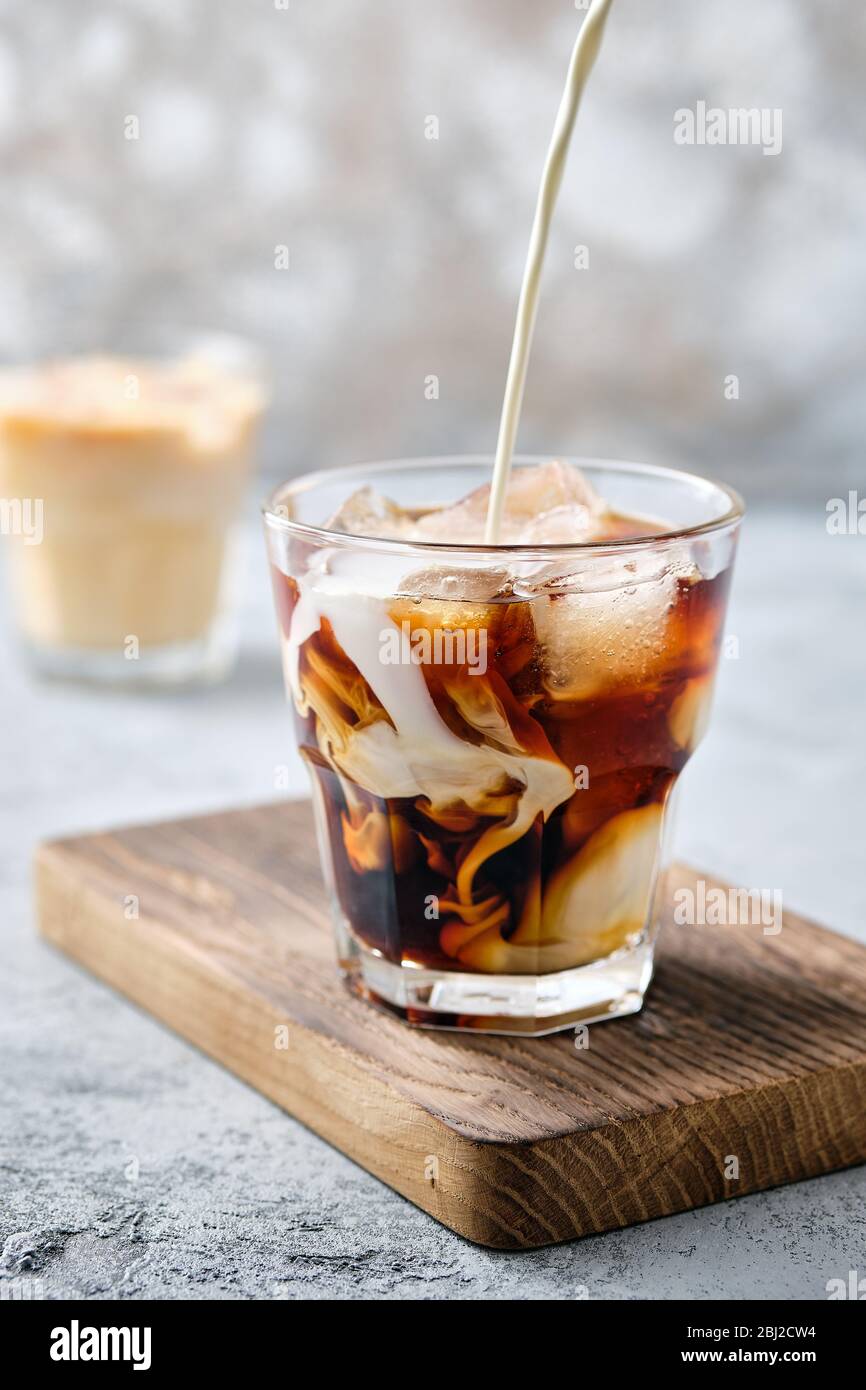 Pouring cream in iced coffee in rocks glass Stock Photo