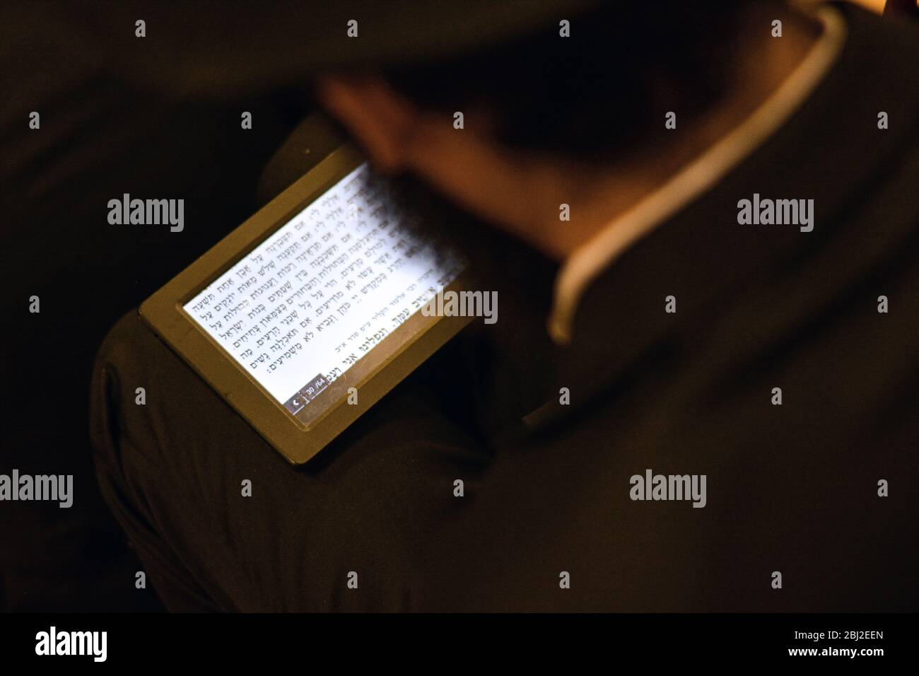 An orthodox Jewish young man reads his Tisha B'Av prayers from a tablet. At a synagogue in Brooklyn, New York City. Stock Photo