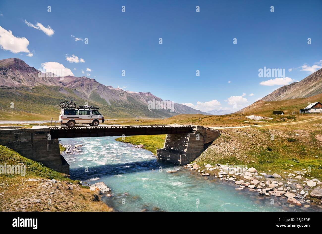 White van with bicycle on the roof is crossing river by bridge in the mountains in Kyrgyzstan Stock Photo