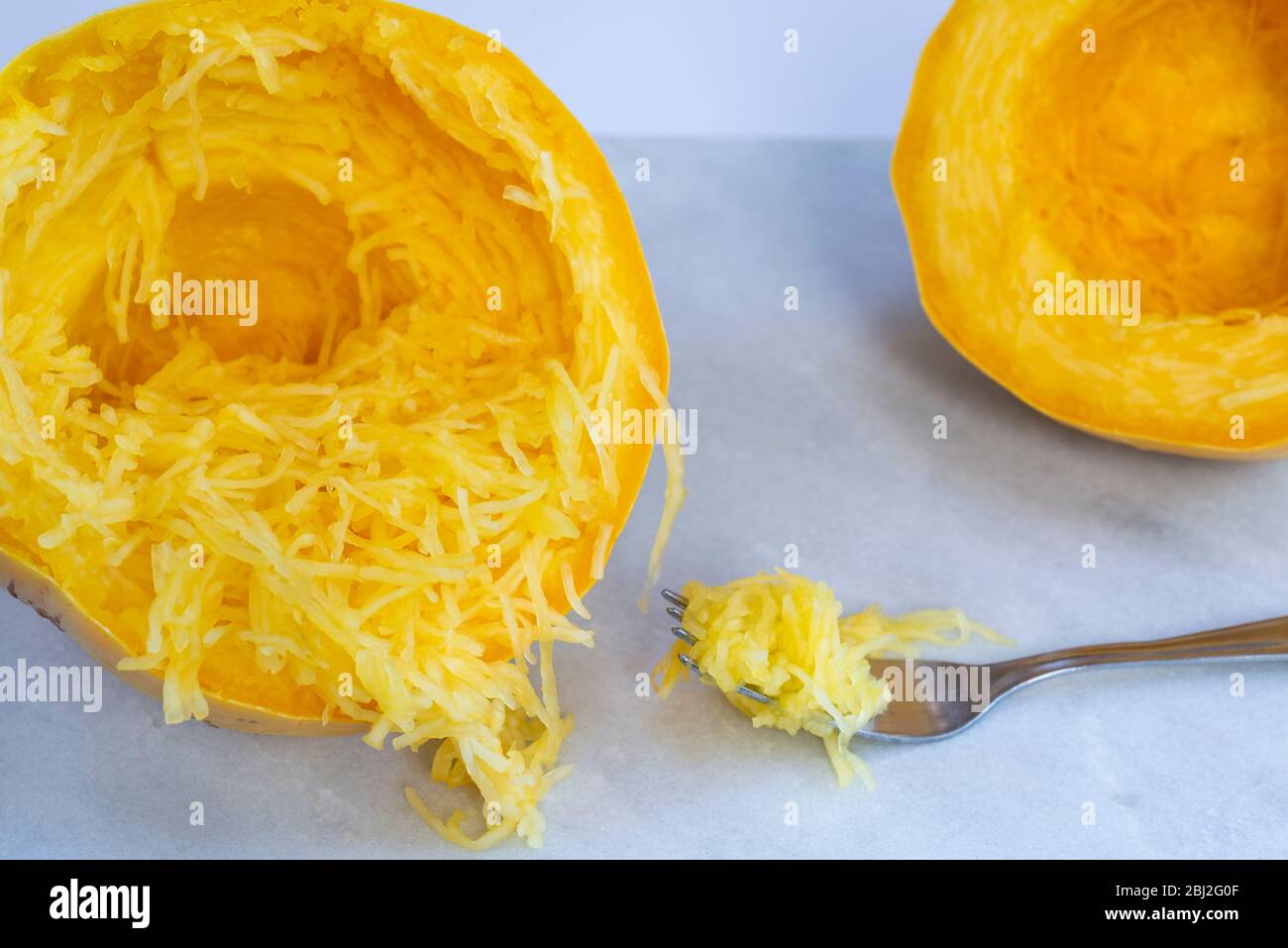 A cooked, halved spaghetti squash, separated into strands with a fork. Stock Photo