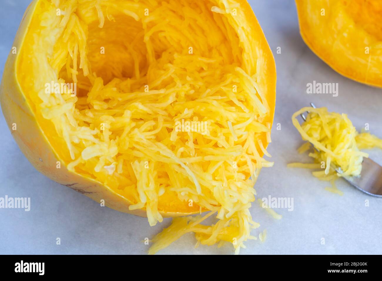 A cooked, halved spaghetti squash, separated into strands with a fork. Stock Photo