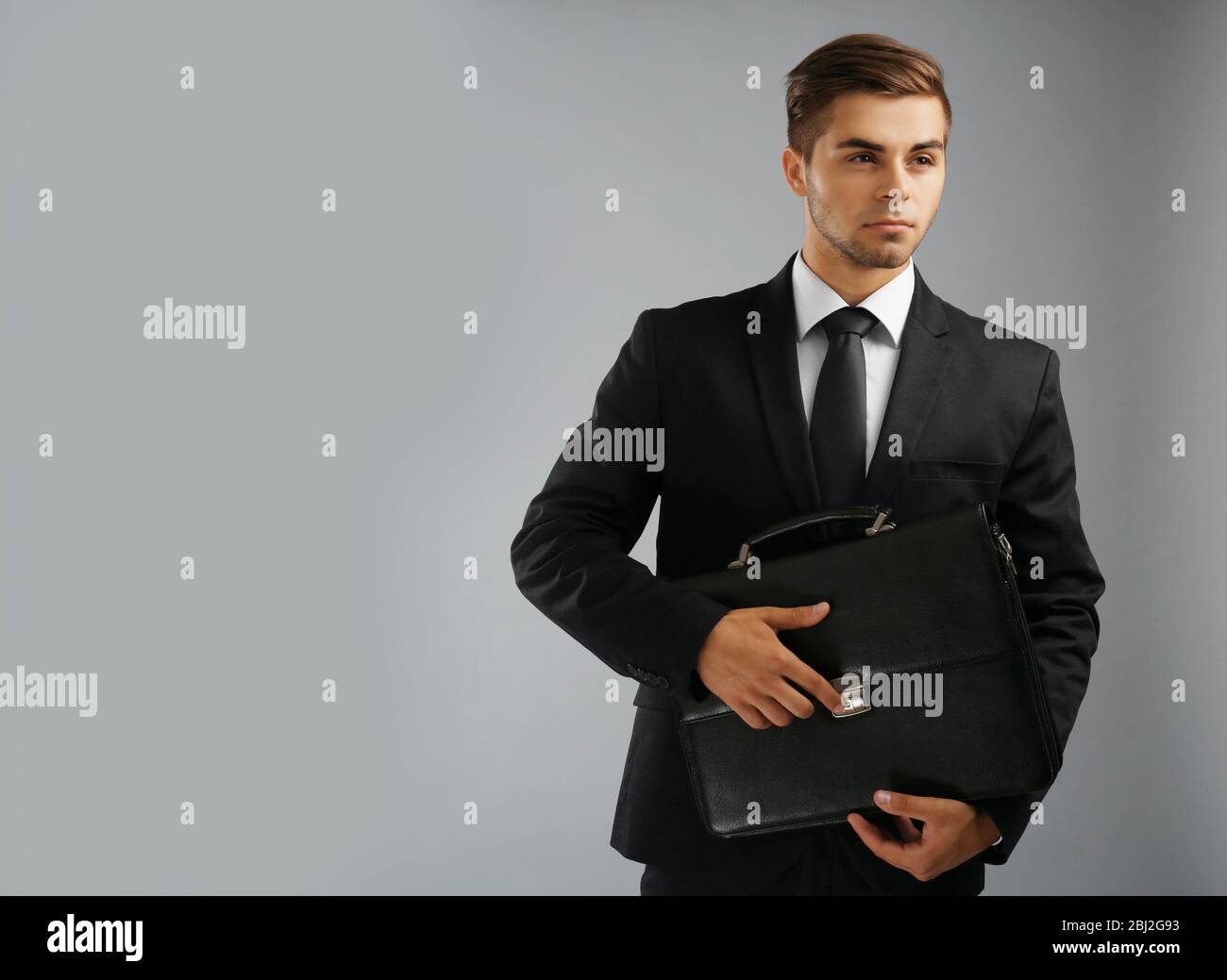 Elegant man in suit with briefcase on gray background Stock Photo - Alamy